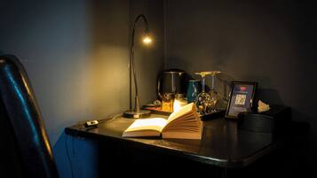 A desk with an open book, a lamp, a mug, and a framed item with a QR code.