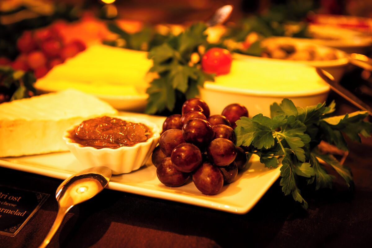 Une table garnie d’une variété d’aliments, notamment du fromage, des raisins et un bol de confiture.