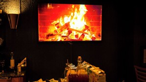 A room with a television displaying a fire, a bar area with bottles and glasses, and a table with food and drinks. - Hotell Aqva Restaurang & Bar – Ett Biosfärhotell med fokus på hållbarhet (Mariestad)