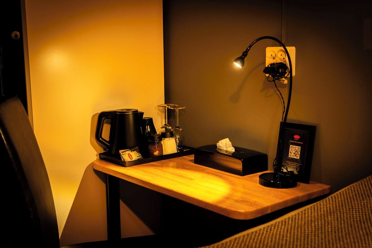 A small workspace with a wooden desk, a coffee machine, a lamp, and a QR code for digital services.