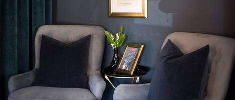 Dos sillones grises con cojines negros, un certificado enmarcado en la pared y un candelabro con velas fijado a la pared.