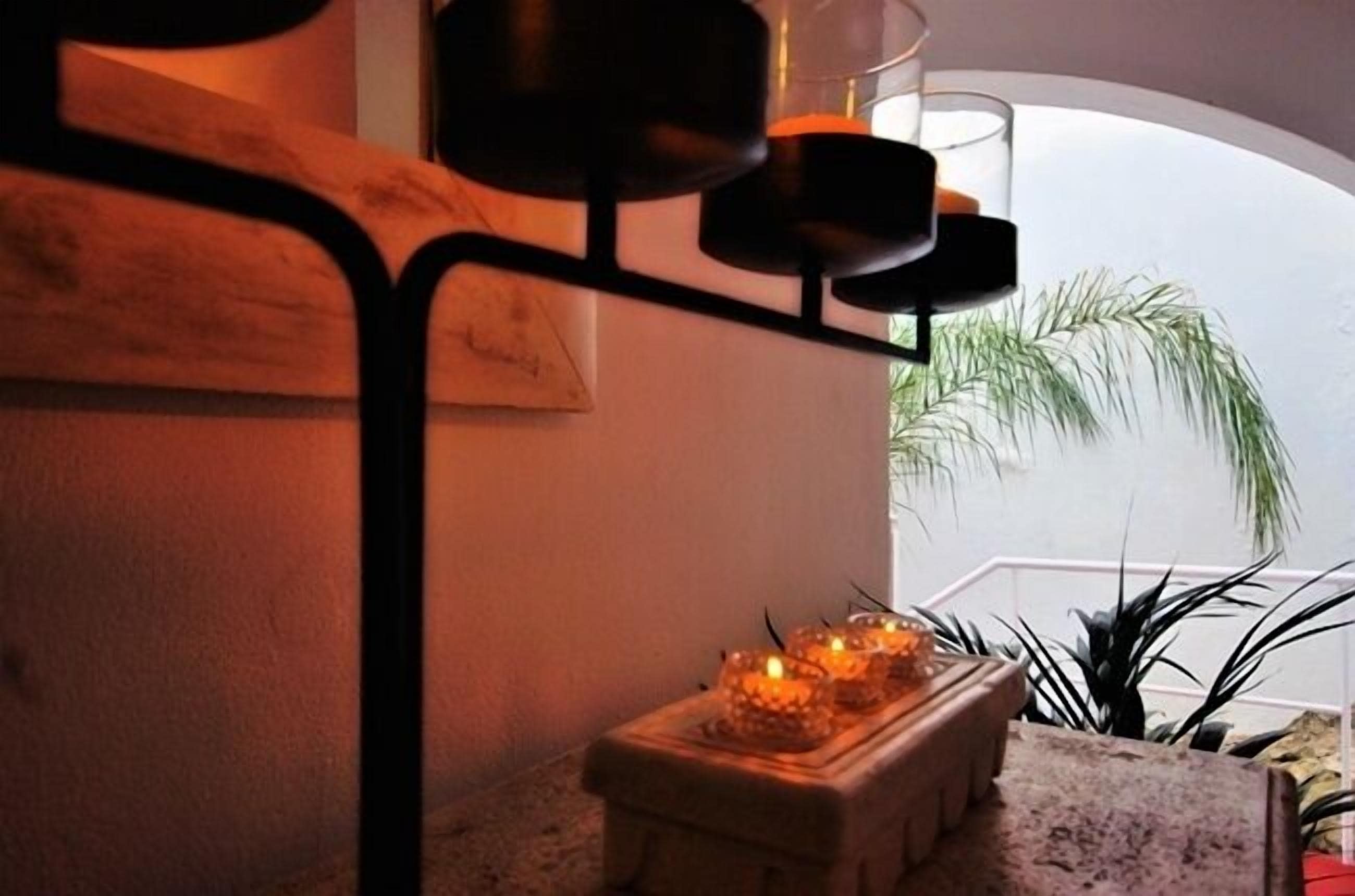 A cozy corner with a small table holding candles, a potted plant, and a view of the outdoors.