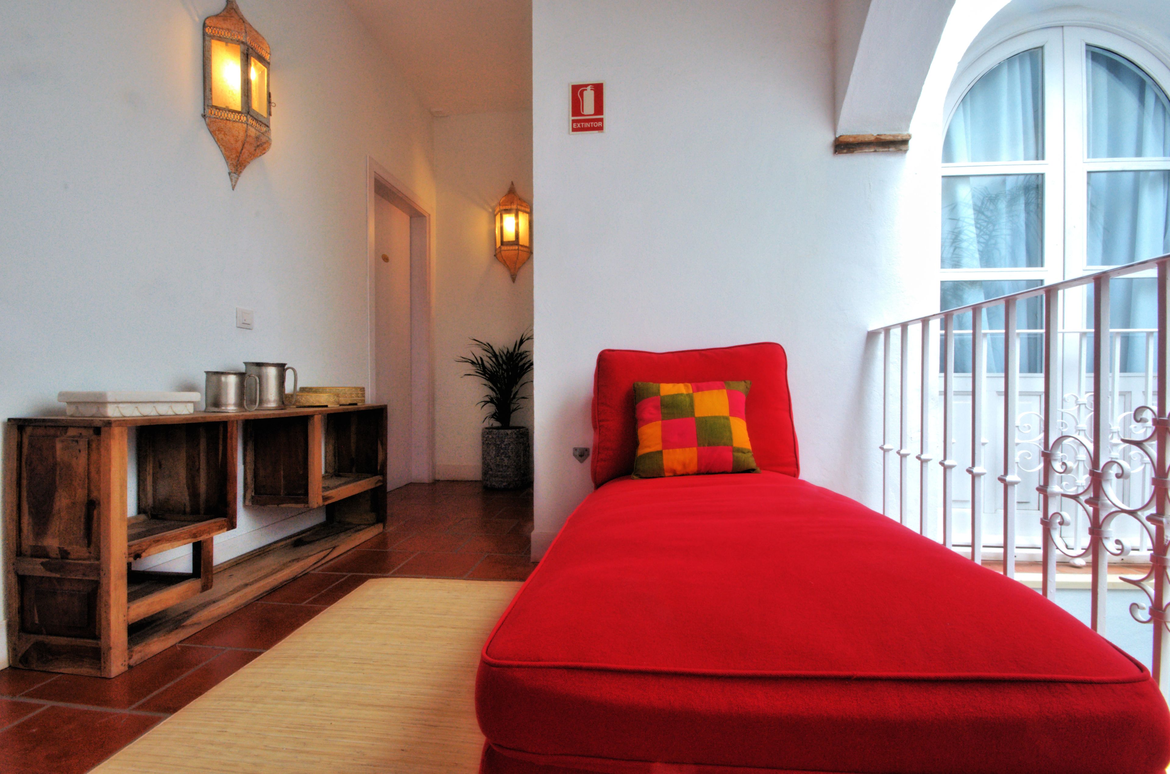 A room with a red bed, wooden shelves, and two wall-mounted lights.