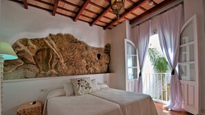 A bedroom with a stone wall, a bed with two pillows, a bedside table, and a balcony with curtains. - Benali Guesthouse (Tarifa)