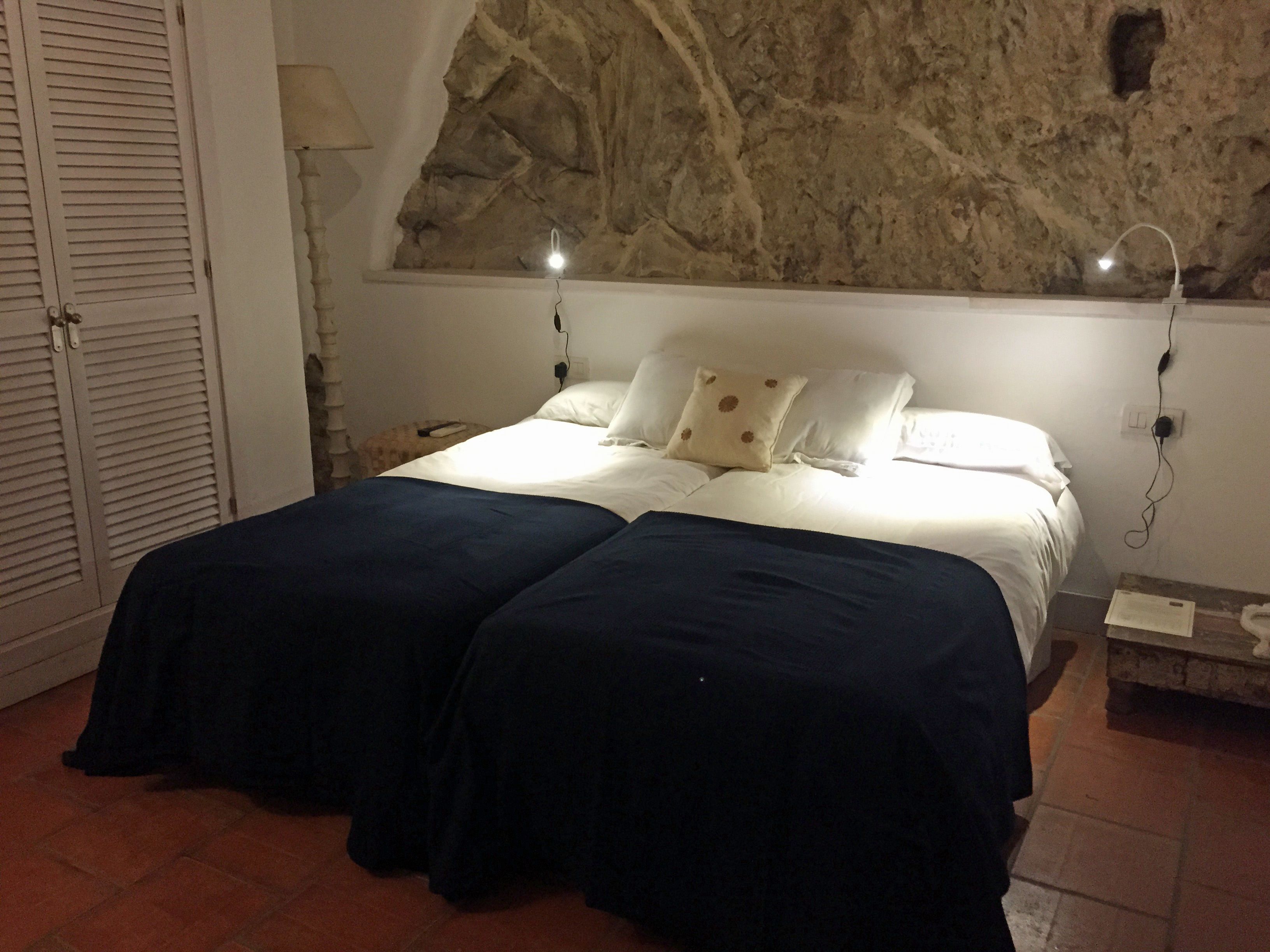 Une chambre avec un mur en pierre, un lit recouvert de draps blancs et une table de chevet.