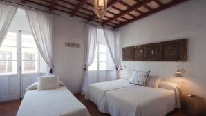 A room with two single beds, white curtains, a wooden ceiling, and a wall-mounted light fixture. - Benali Guesthouse (Tarifa)
