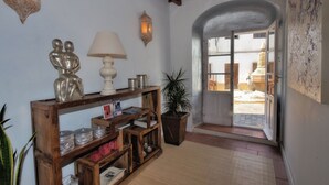 A hallway with a wooden console table, a white lamp, decorative wall sconces, a potted plant, and an open door leading to a bright outdoor area. - Benali Guesthouse (Tarifa)