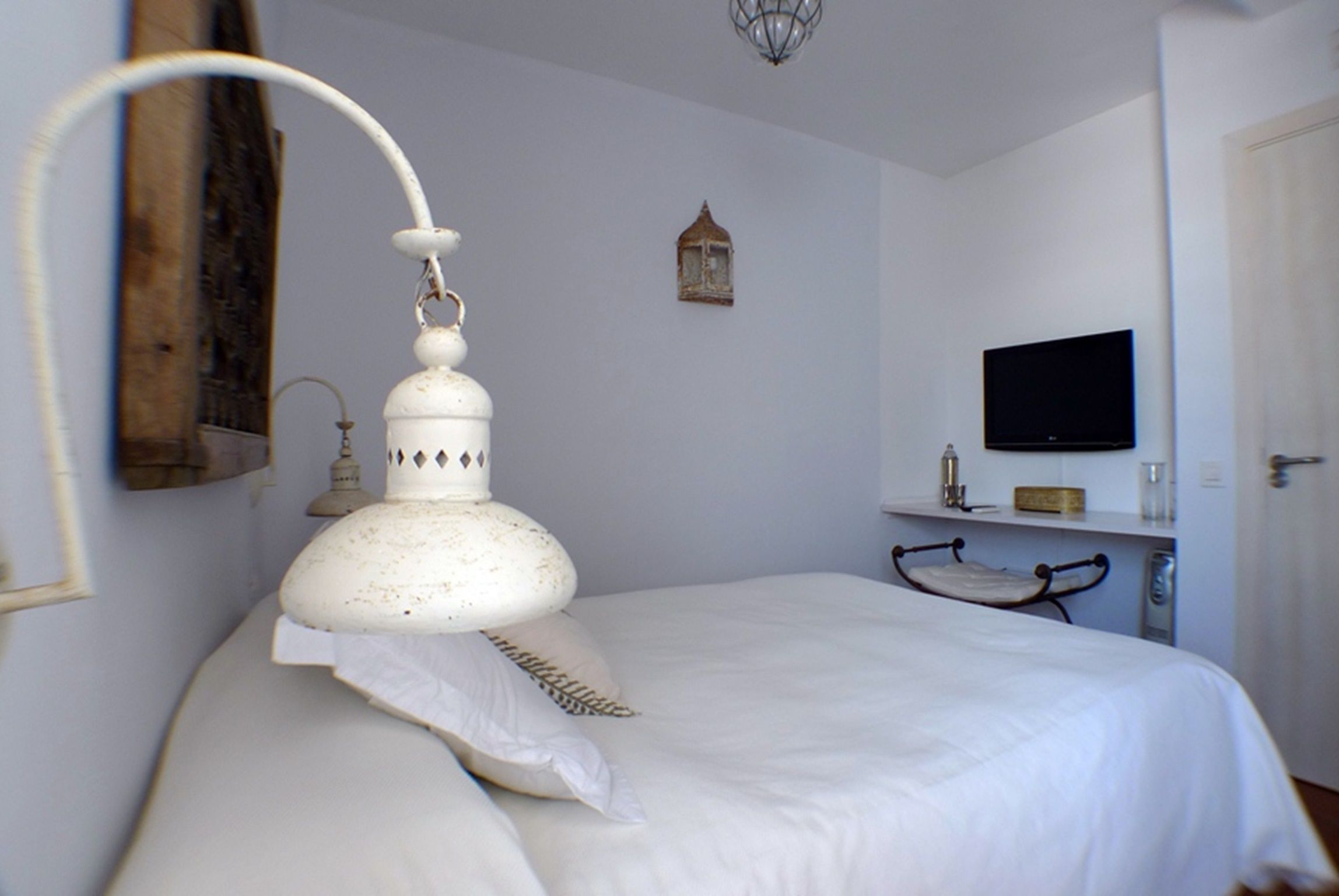 Un dormitorio con cama, televisión instalada en la pared, estante con espejo y lámpara colgante.