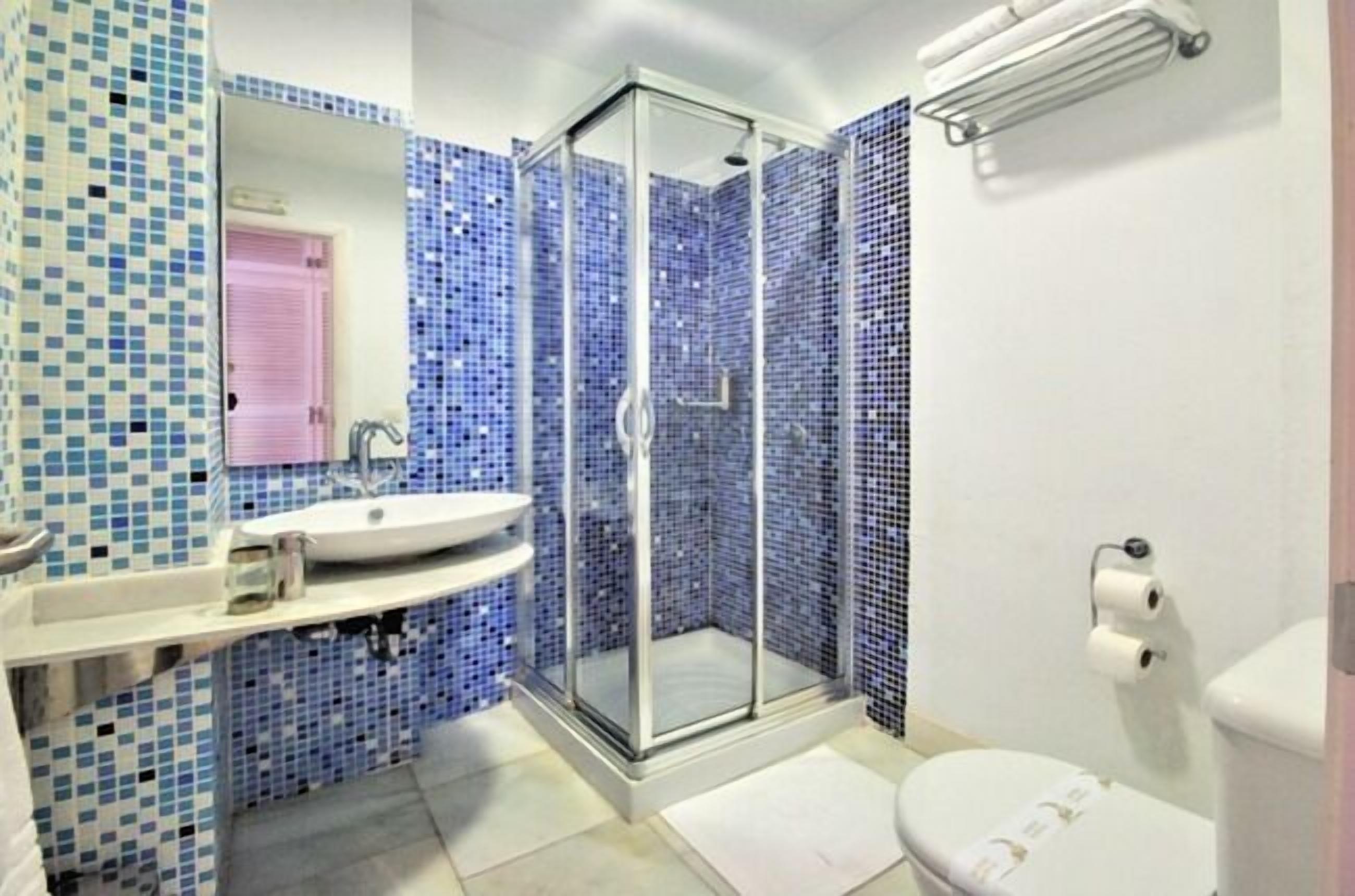 Un baño con ducha envuelta en vidrio, lavamanos e inodoro.