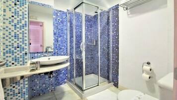 Un baño con ducha envuelta en vidrio, lavamanos e inodoro.