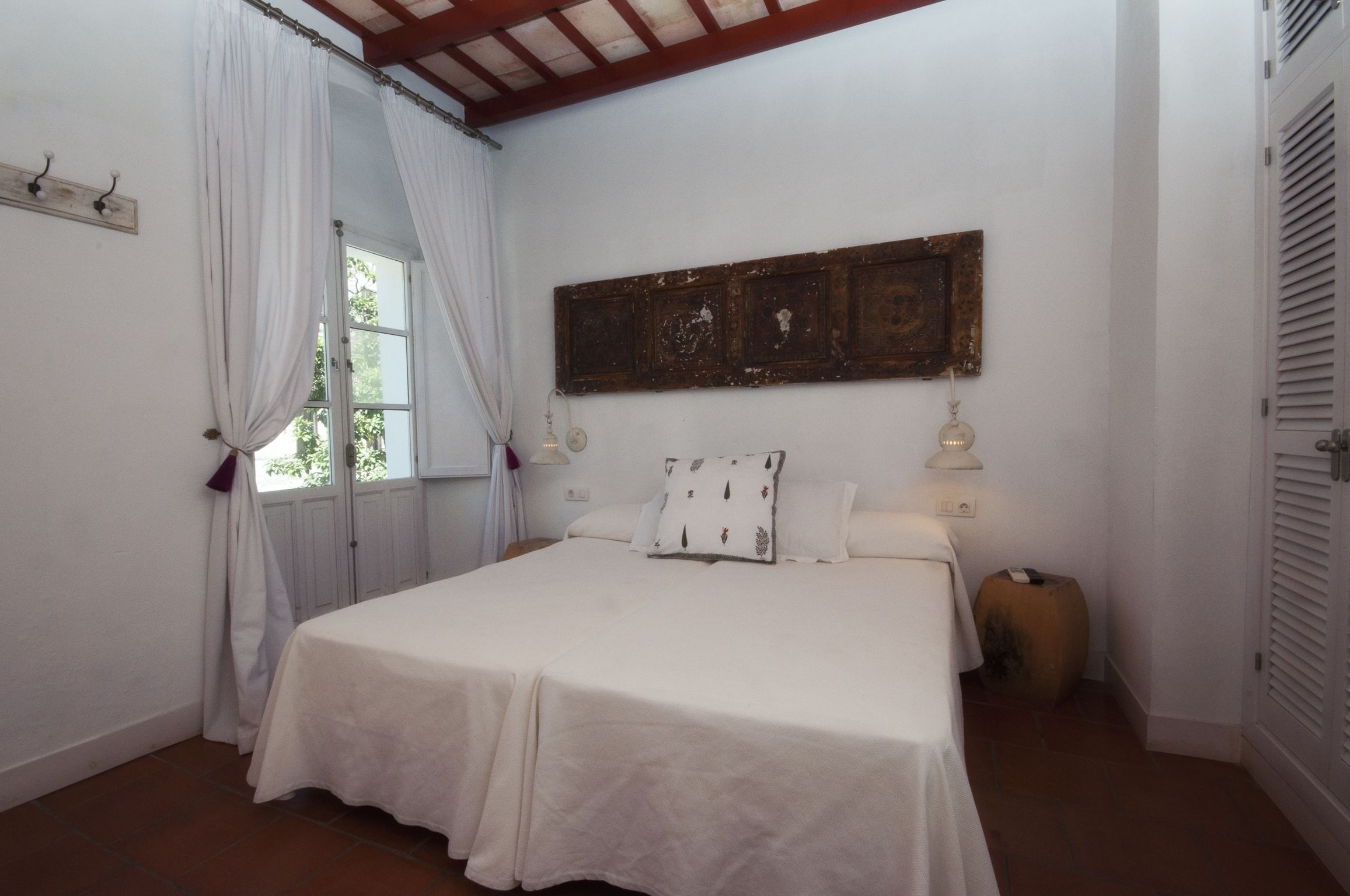 Une chambre à coucher avec un lit, des rideaux, un tableau accroché au mur et une table de chevet.