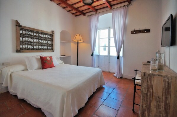 A bedroom with a bed, a lamp, a window with curtains, a wooden table, and a wall-mounted TV. - Benali Guesthouse (Tarifa)