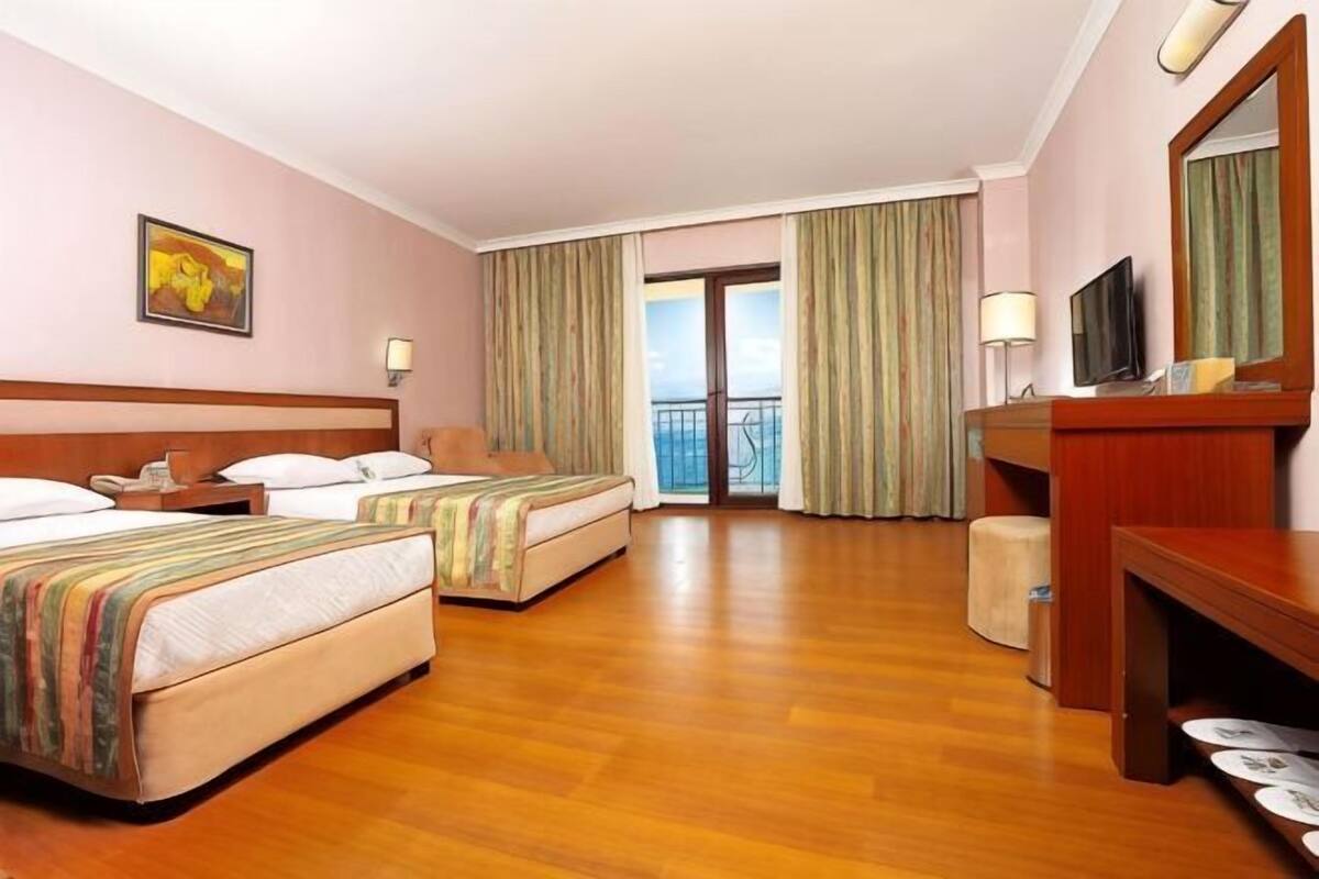 A hotel room with two beds, a desk, a TV, and a balcony with curtains.