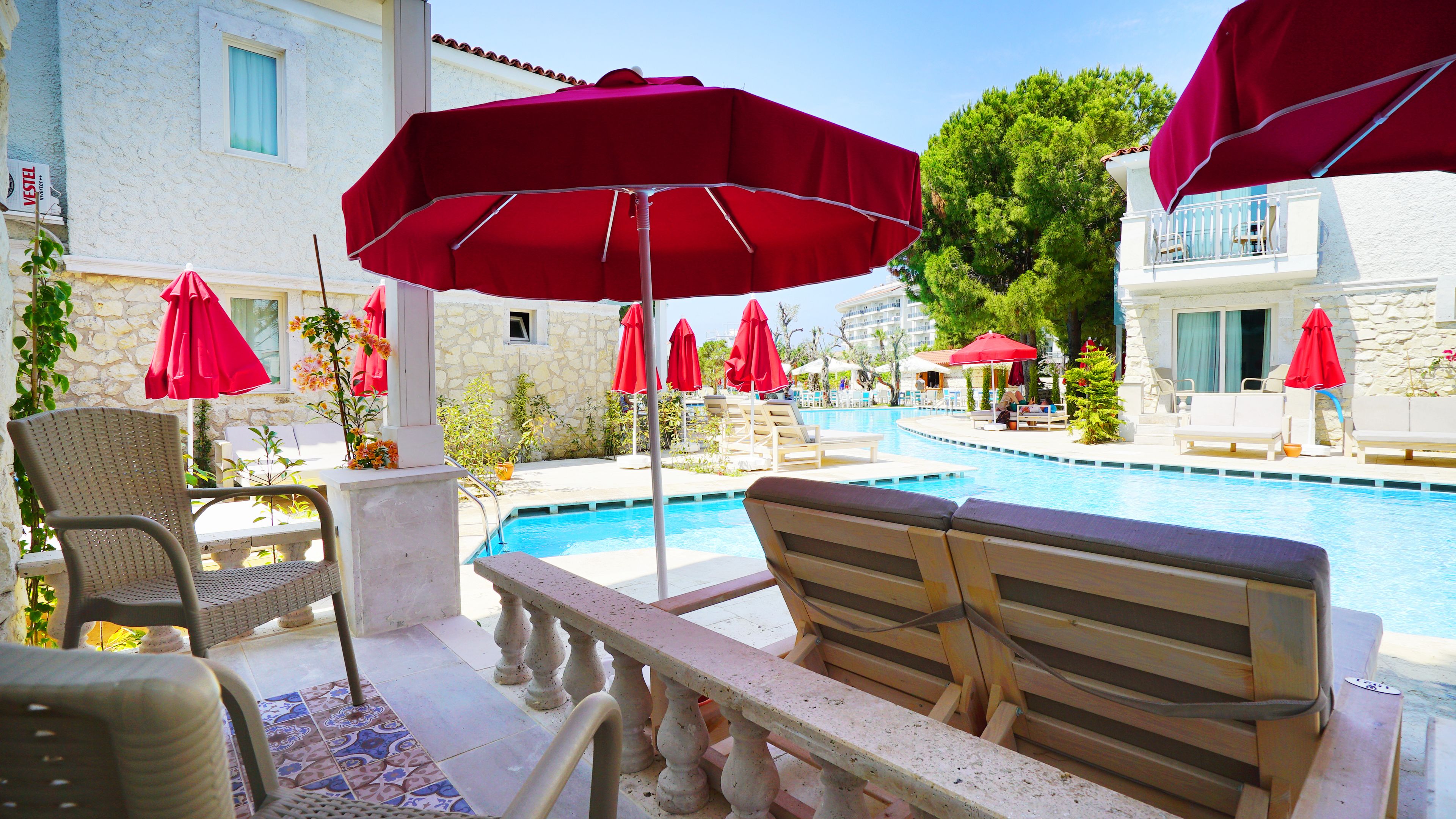 A poolside area with lounge chairs, red umbrellas, and a stone building in the background.