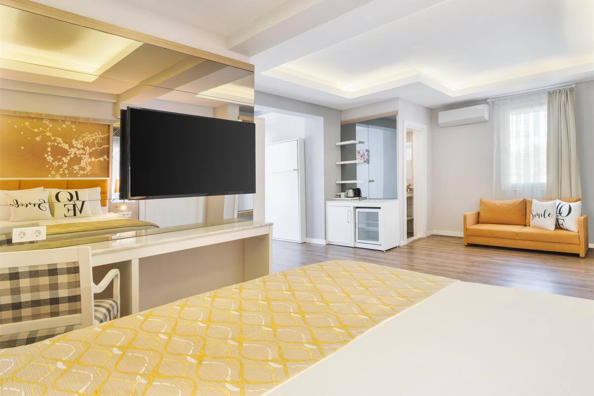 A modern living room with a sofa, a television, and a kitchen area.