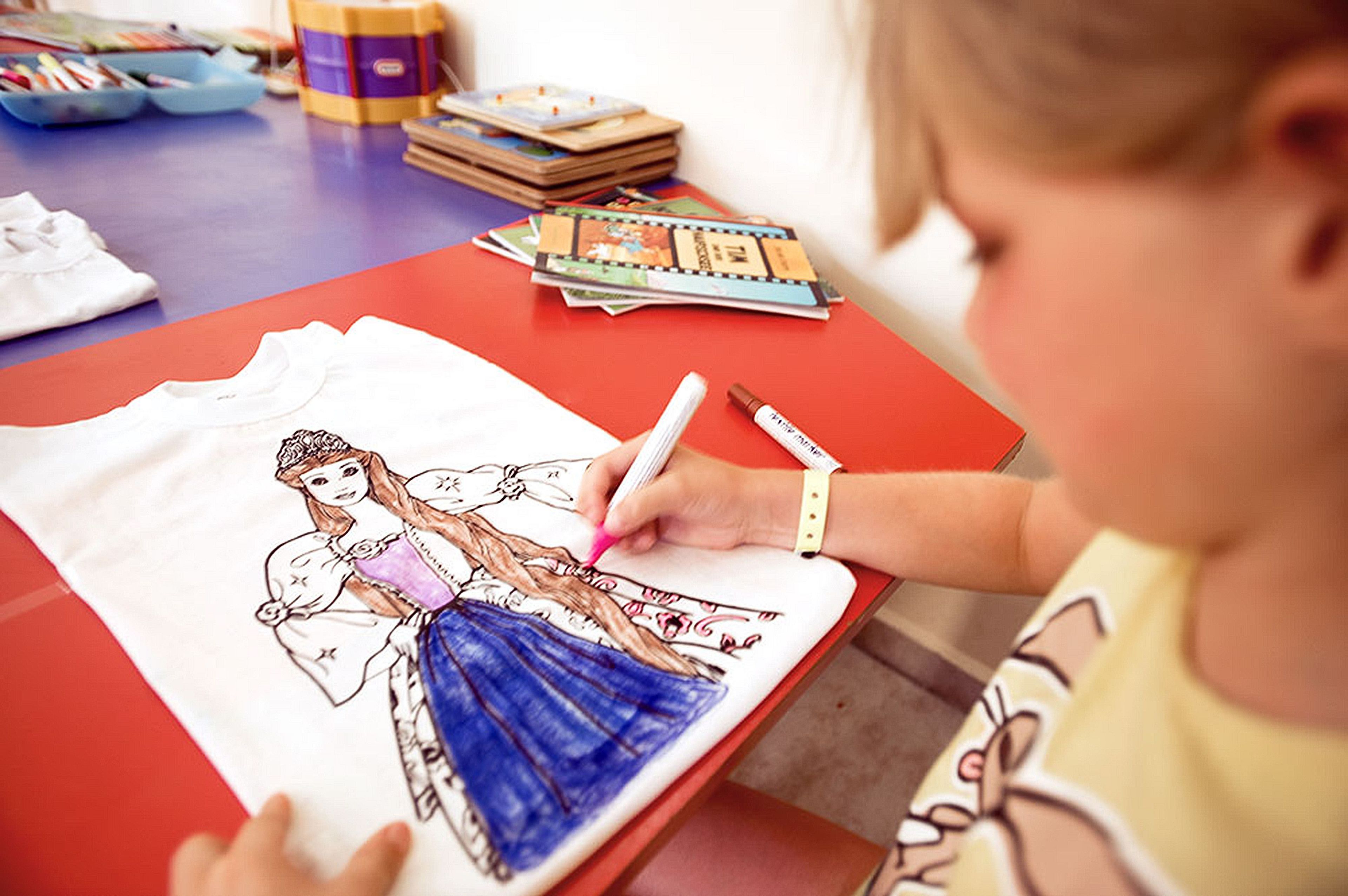 A child coloring a drawing on a white shirt.