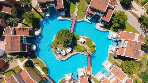 An aerial view of a resort with a central swimming pool surrounded by villas, palm trees, and a well-maintained lawn. - Selectum Family Comfort Side (Manavgat)