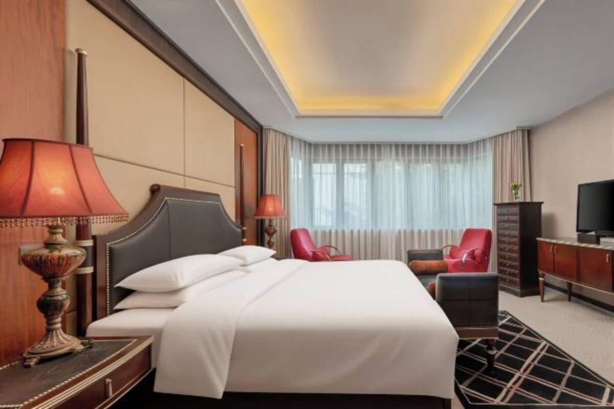 A hotel room with a large bed, two bedside lamps, a television, a desk, and a chair.