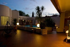 Uma área de piscina com hidromassagem, plantas em vasos e uma cadeira balanço.
