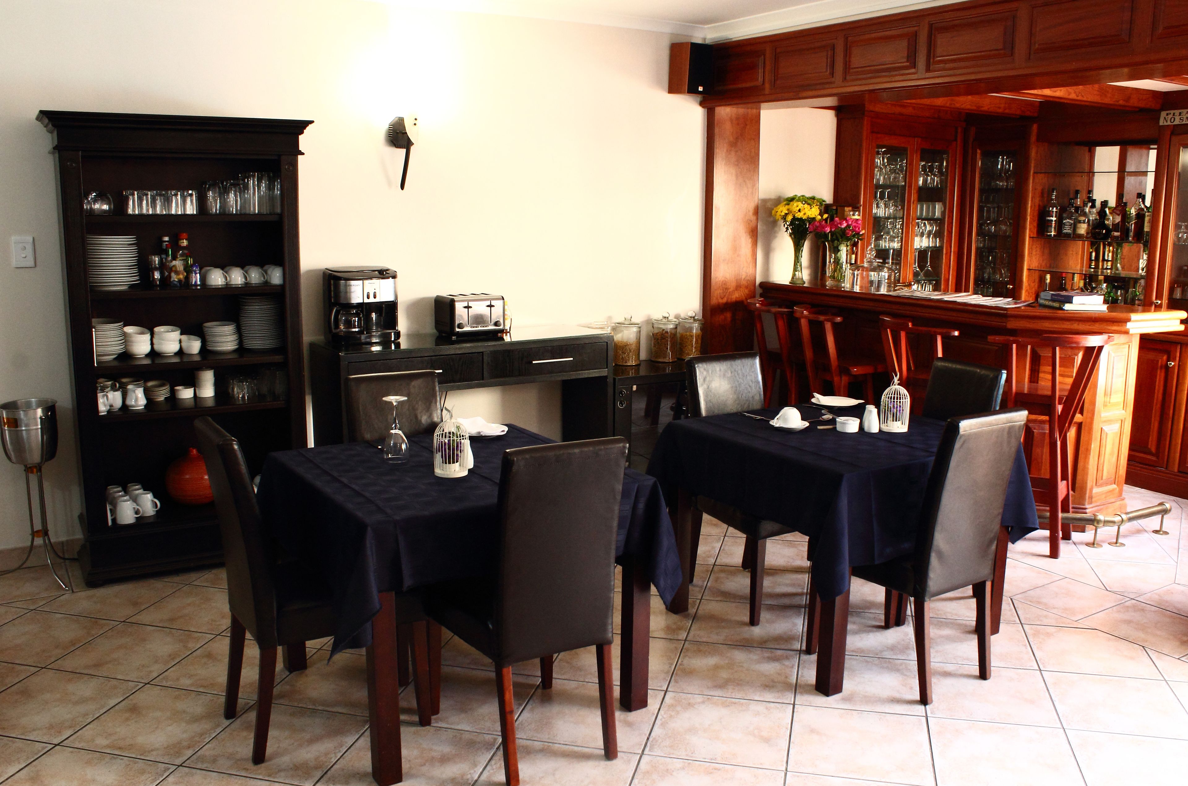 Comedor con dos mesas dispuestas para cuatro, una máquina de café y una zona de bar con una bodega y botellas.