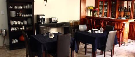 Comedor con dos mesas dispuestas para cuatro, una máquina de café y una zona de bar con una bodega y botellas.