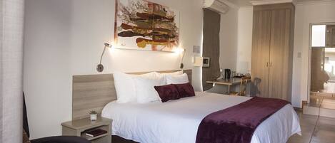 A modern hotel room with a large bed, a desk, and a wardrobe.