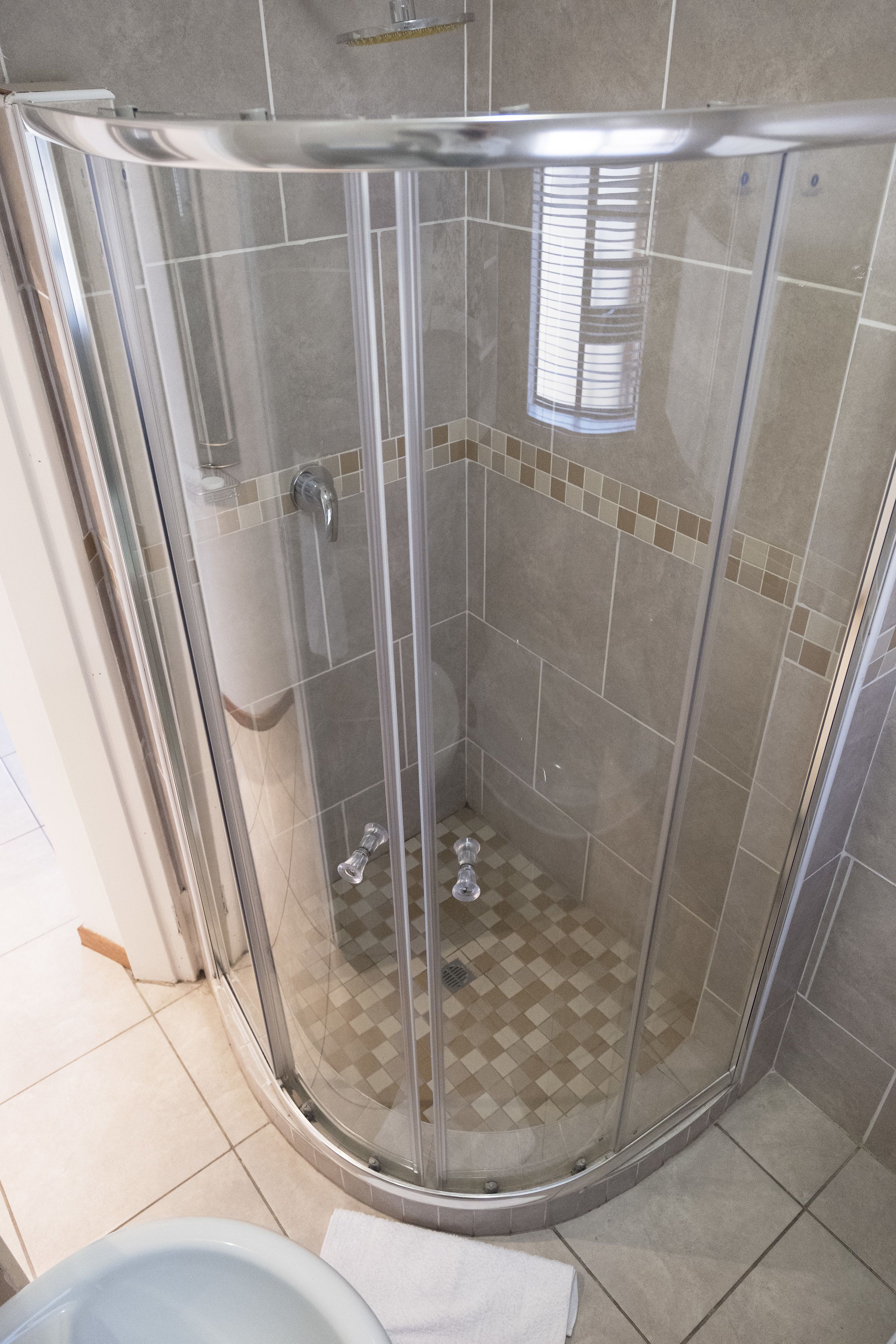 A glass-enclosed shower stall with a checkered floor pattern, a white toilet, and a towel on the floor.