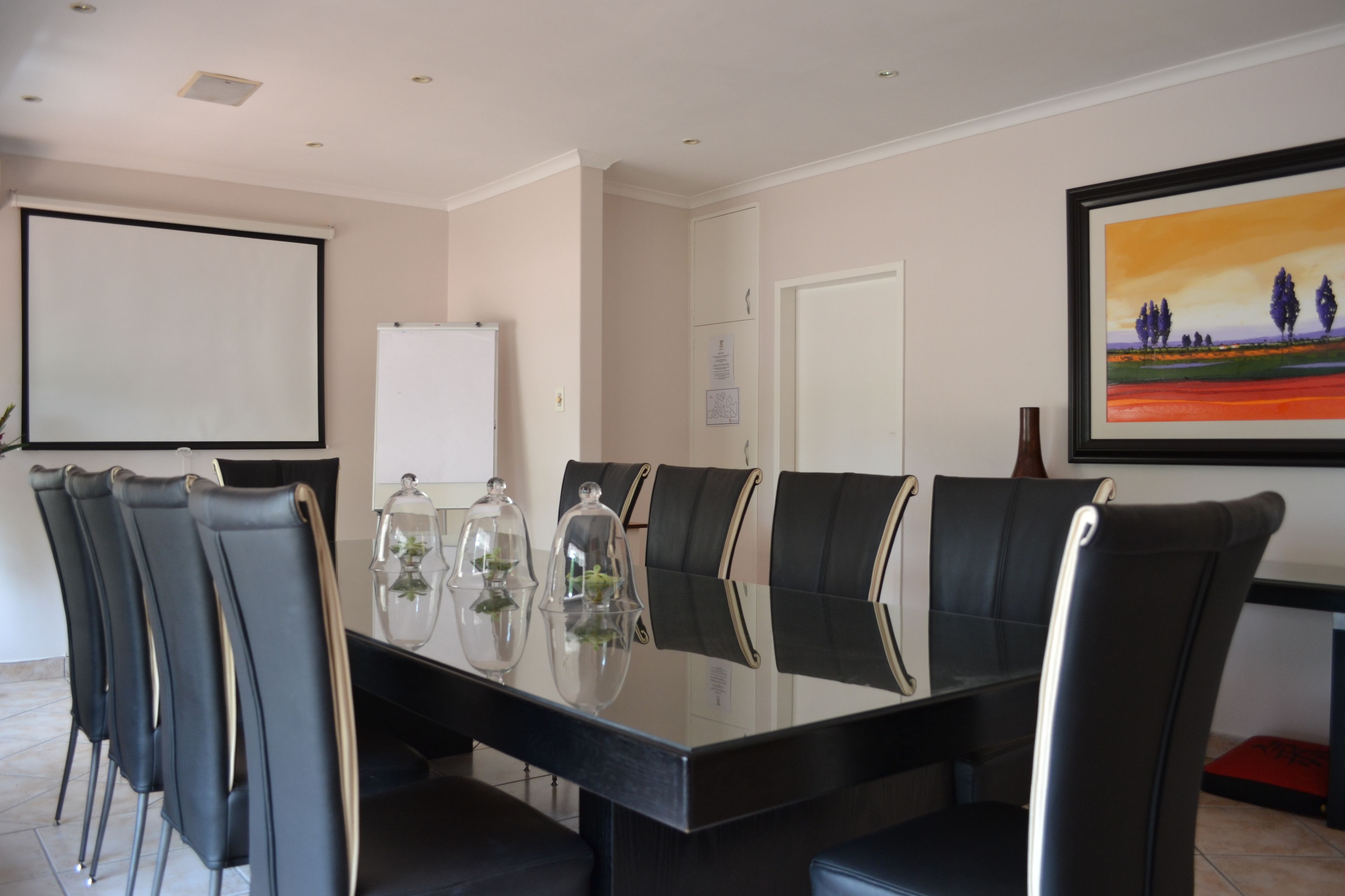 A conference room with a glass table, black chairs, a whiteboard, and a framed painting on the wall.