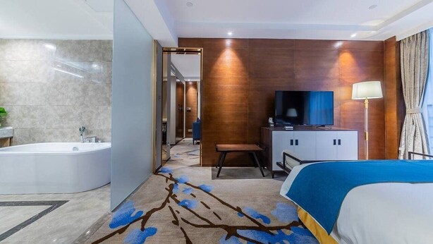 Ein modernes Hotelzimmer mit einem großen Bett, einem Fernseher, einem Schreibtisch und einem Badezimmer mit einer Badewanne.