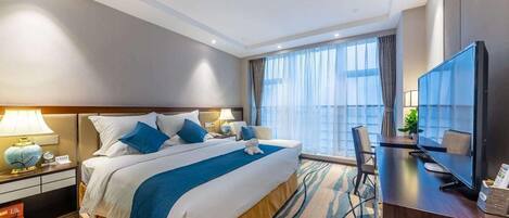 A hotel room with a large bed, a desk with a TV, and a view of the city through the window.