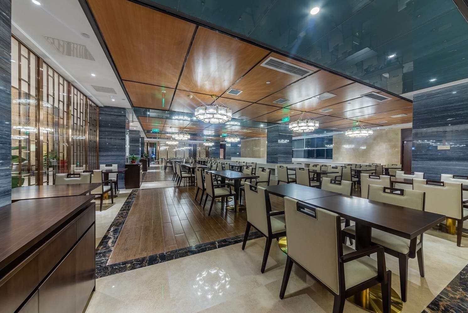 A spacious restaurant with high ceilings, modern chandeliers, and a mix of wooden and marble flooring.