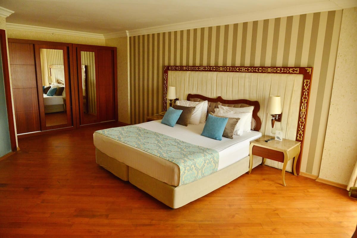 A hotel room with a large bed, wooden floor, striped wallpaper, and a mirror in the closet.