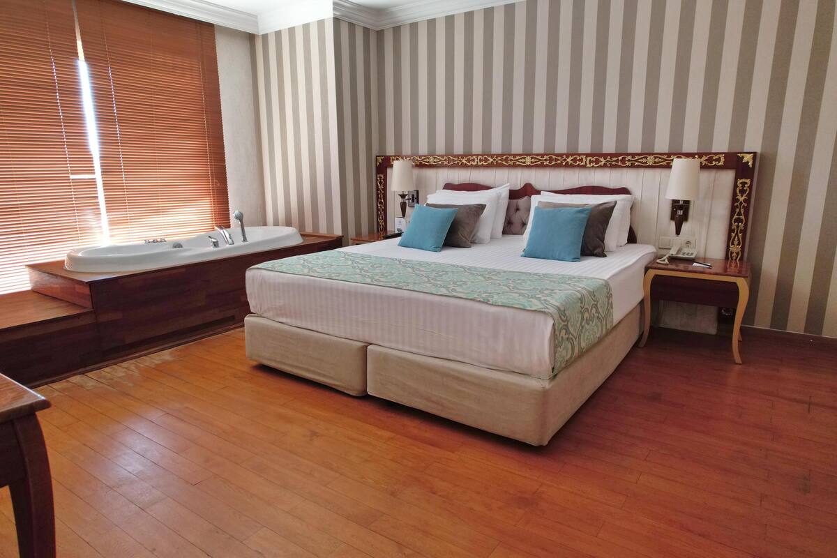 A hotel room with a large bed, a bathroom with a bathtub, and a wooden floor.