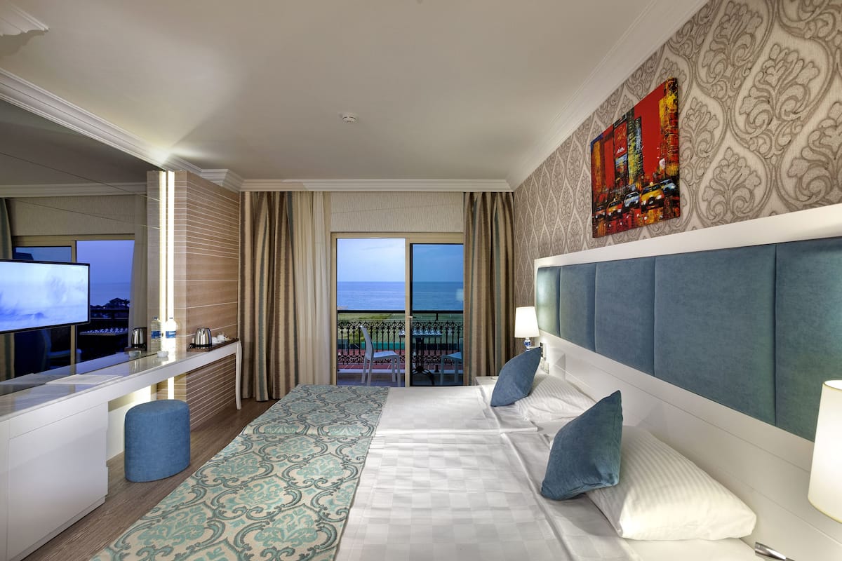 A hotel room with a large bed, a desk with a TV, a balcony with a view, and a decorative wall piece.