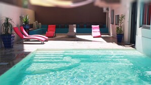 Zona de piscina con sillones de descanso y plantas en macetas.