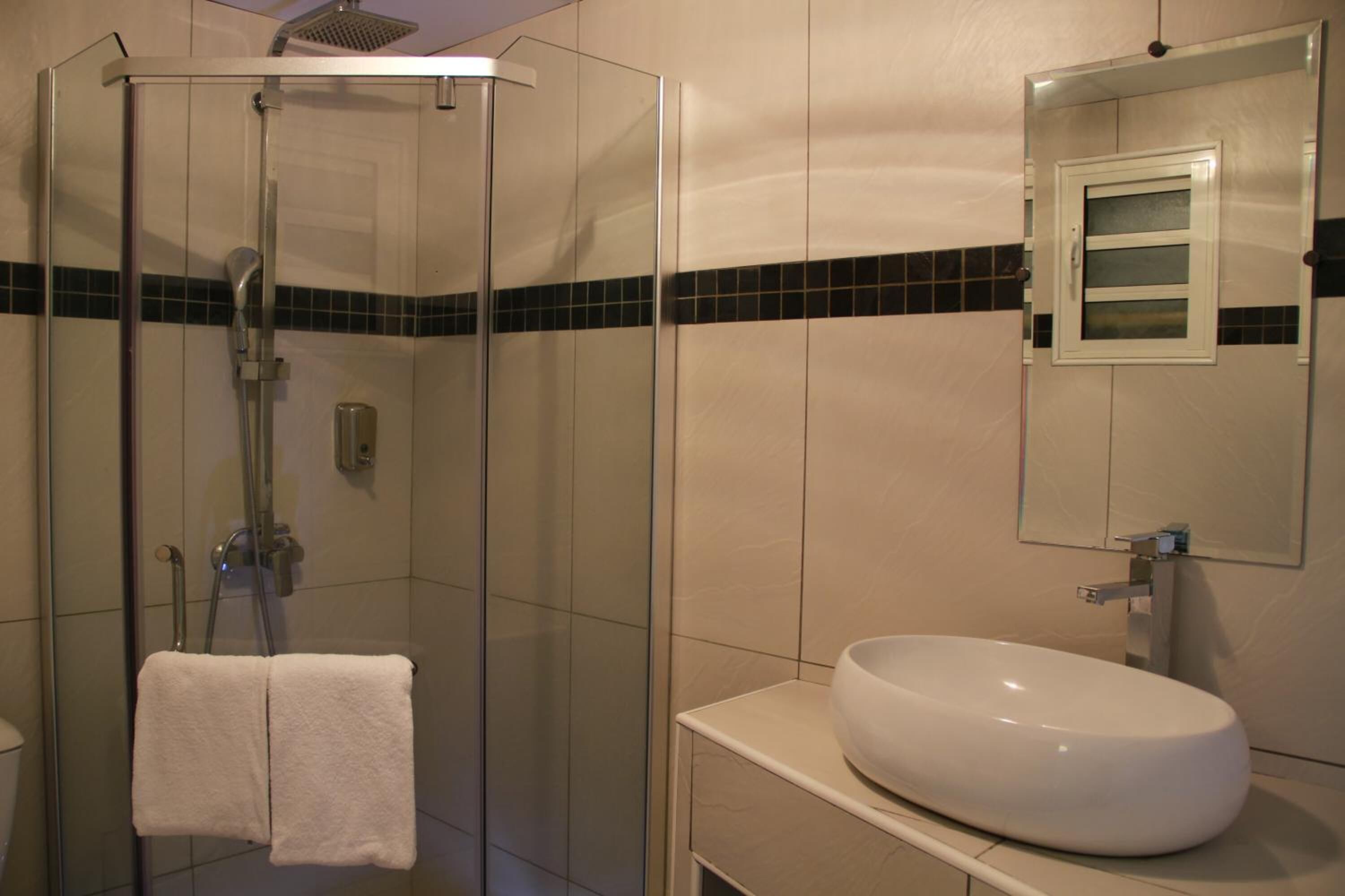 Uma casa de banho com chuveiro envidraçado, lavatório branco e espelho sobre o lavatório.
