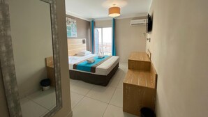 Una habitación de hotel con una cama, un escritorio de madera, un espejo y una lámpara en el techo.