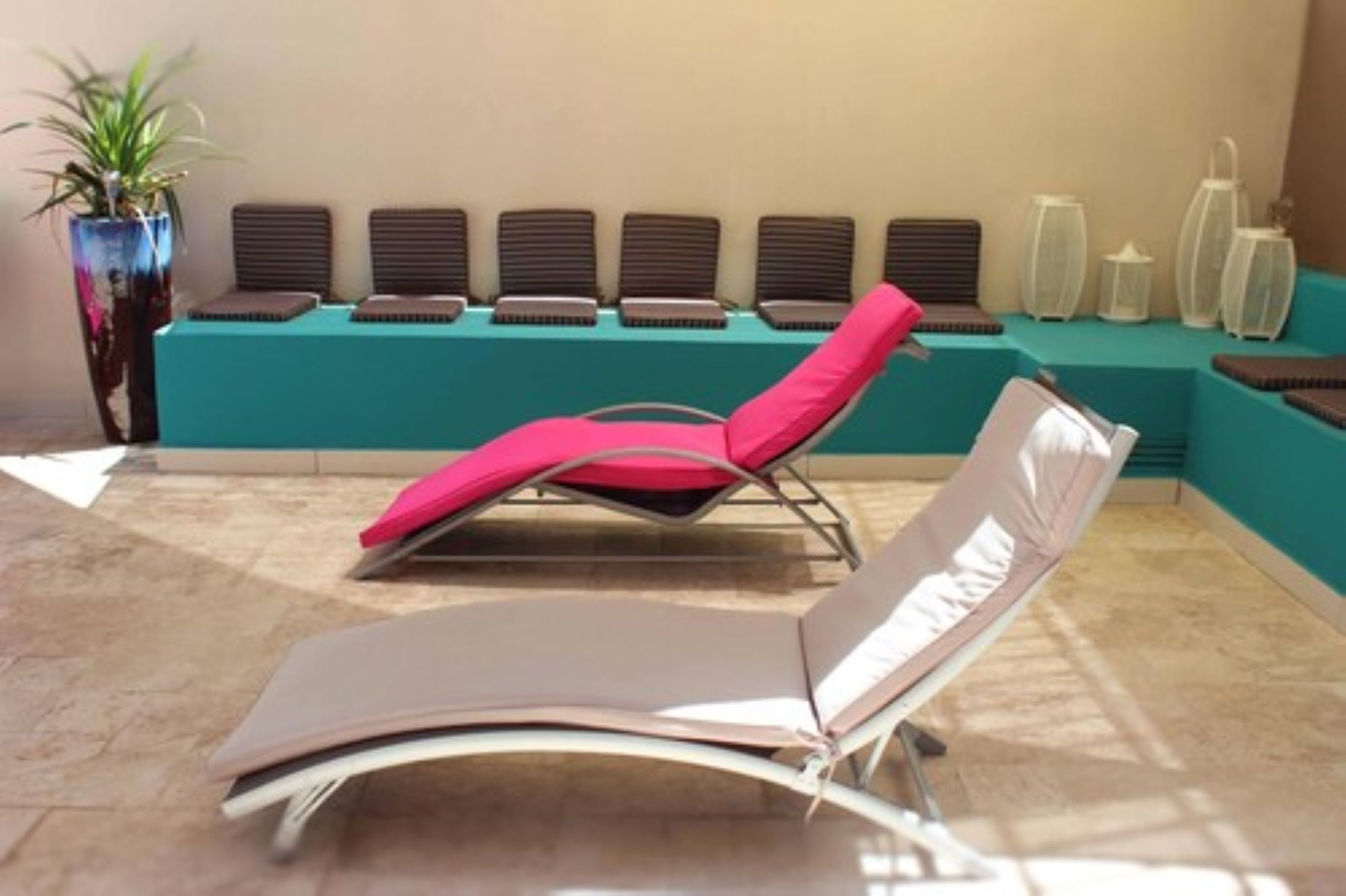 A sunlit room with a teal reception desk, multiple lounge chairs, and a potted plant.
