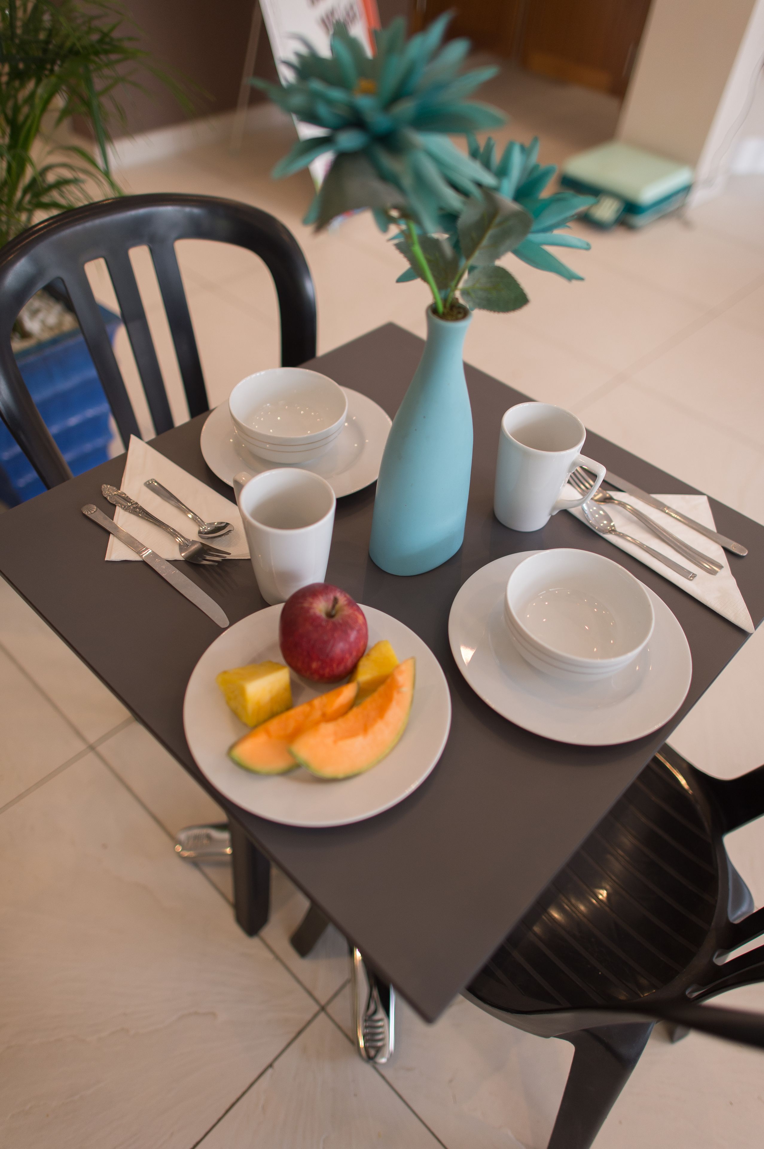 Uma mesa de jantar com pratos, tigelas, talheres e um vaso com planta.