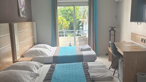 Habitación de hotel con dos camas, un escritorio, una silla y un balcón con vista a zonas verdes.