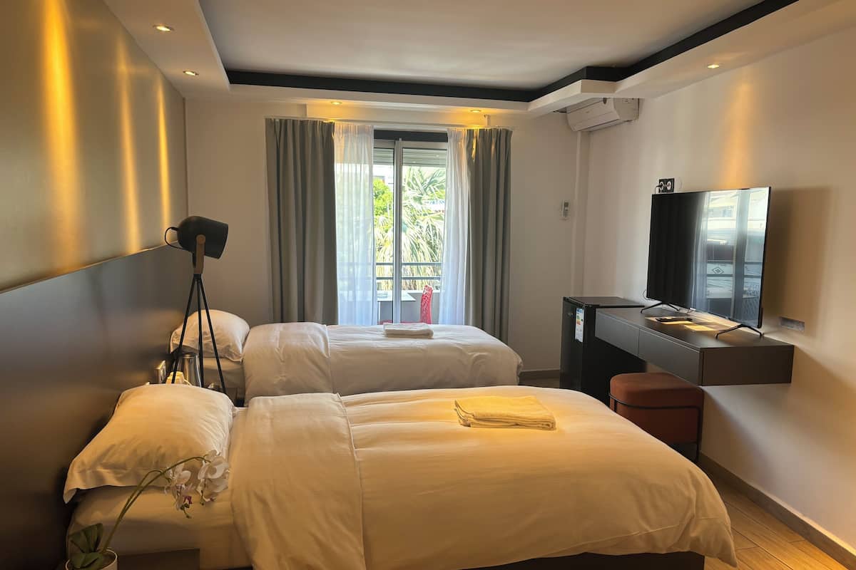 Una habitación de hotel moderna con dos camas, un escritorio con televisor de pantalla plana y un balcón con cortinas.