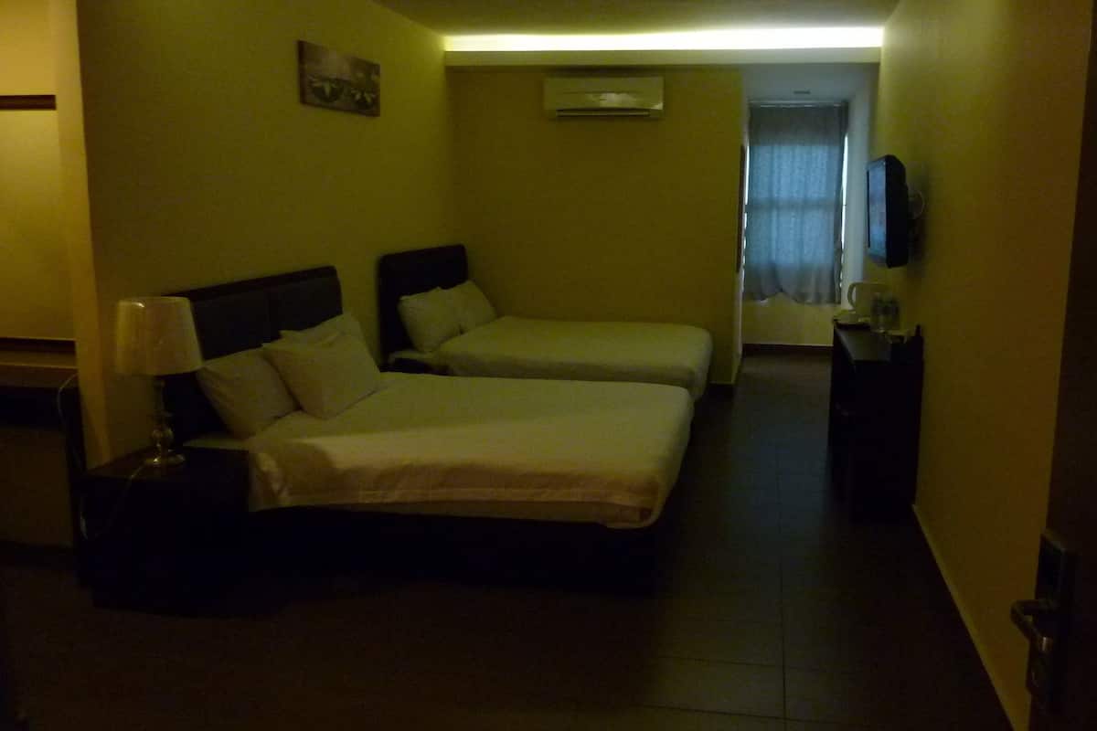 Una habitación de hotel con dos camas, una mesita de noche con lámpara, un televisor de pantalla plana y un equipo de aire acondicionado en la pared.