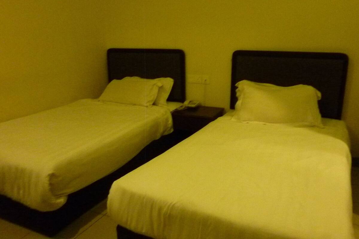 Dos camas individuales con sábanas blancas en una habitación con paredes amarillas.