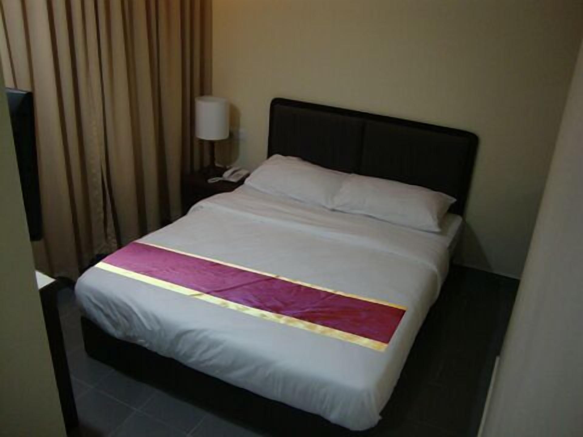A hotel room with a bed, a nightstand, a lamp, and a curtain.