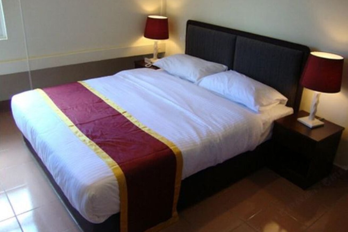 A hotel room with a large bed, two bedside lamps, and a wooden floor.