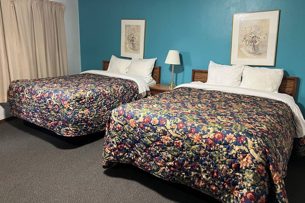 Habitación de hotel con dos camas, cada una con ropa de cama floral, una mesita de noche con lámpara y dos cuadros enmarcados en la pared.