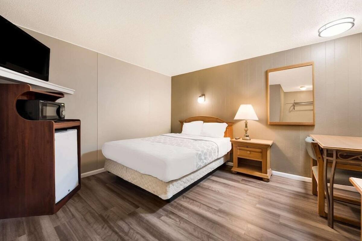 A hotel room with a bed, a desk, a chair, a TV, and a microwave.