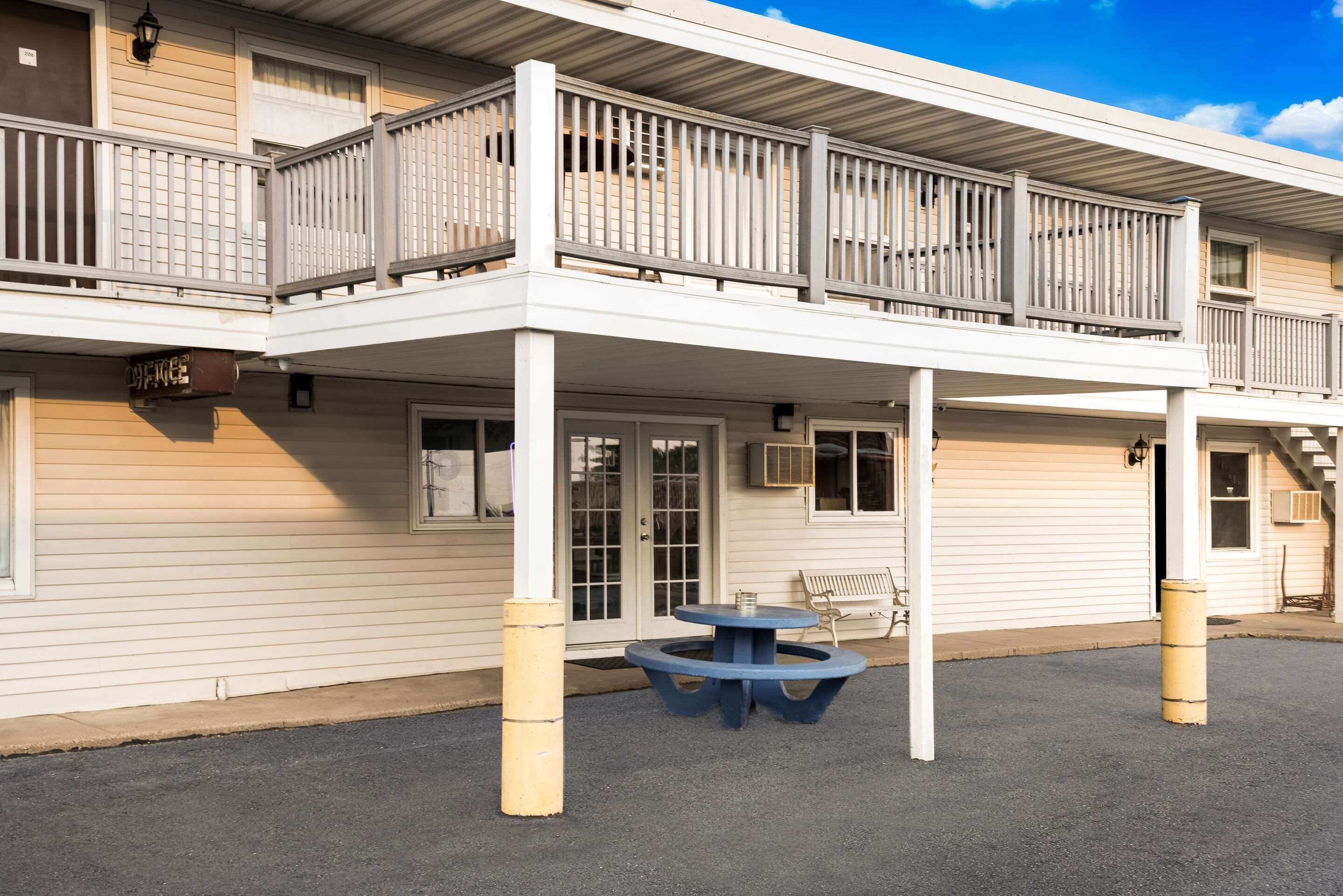 A two-story building with a balcony, a small table, and a bench outside.