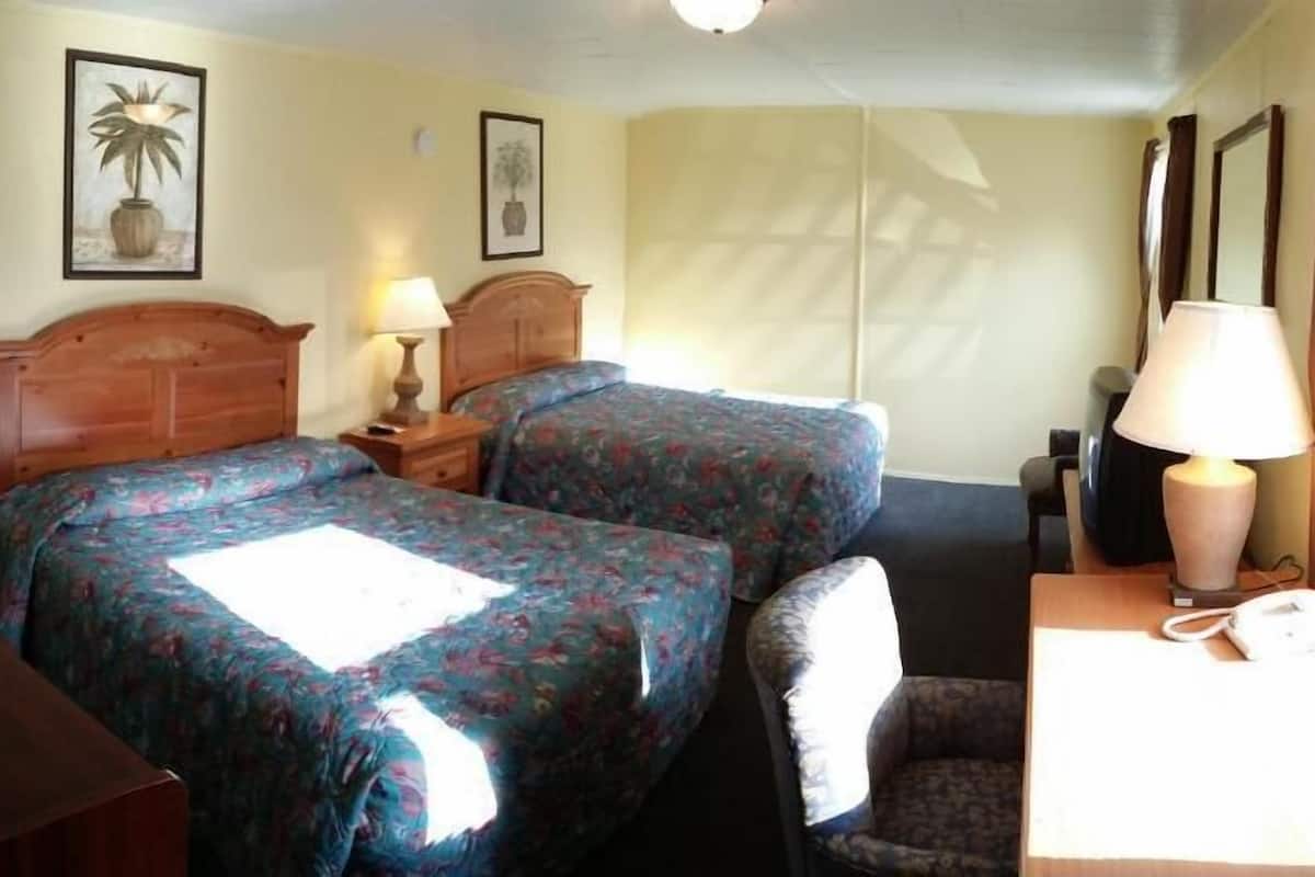 A hotel room with two beds, a desk with a chair, a lamp, and two framed pictures on the wall.