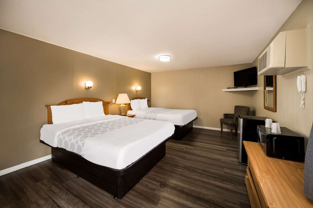 A hotel room with two beds, a desk, a chair, a TV, and a phone.
